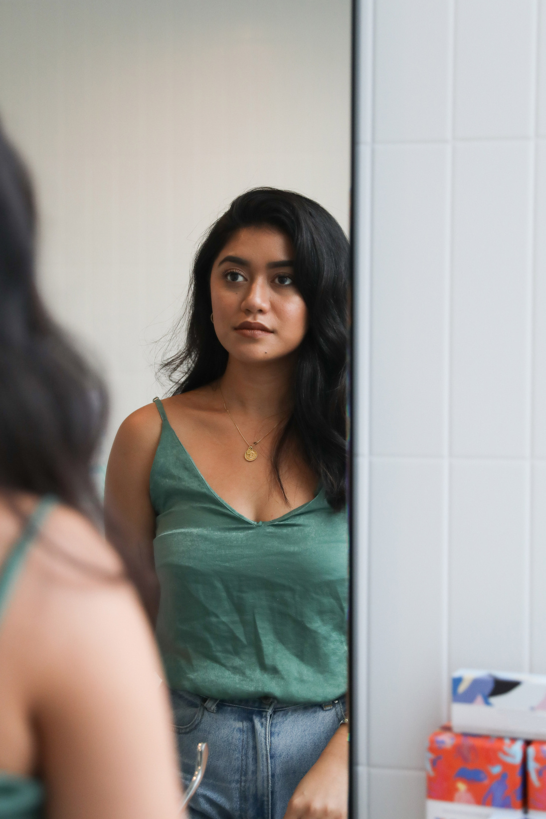 Woman looking at self in mirror in office toilet with free tampons