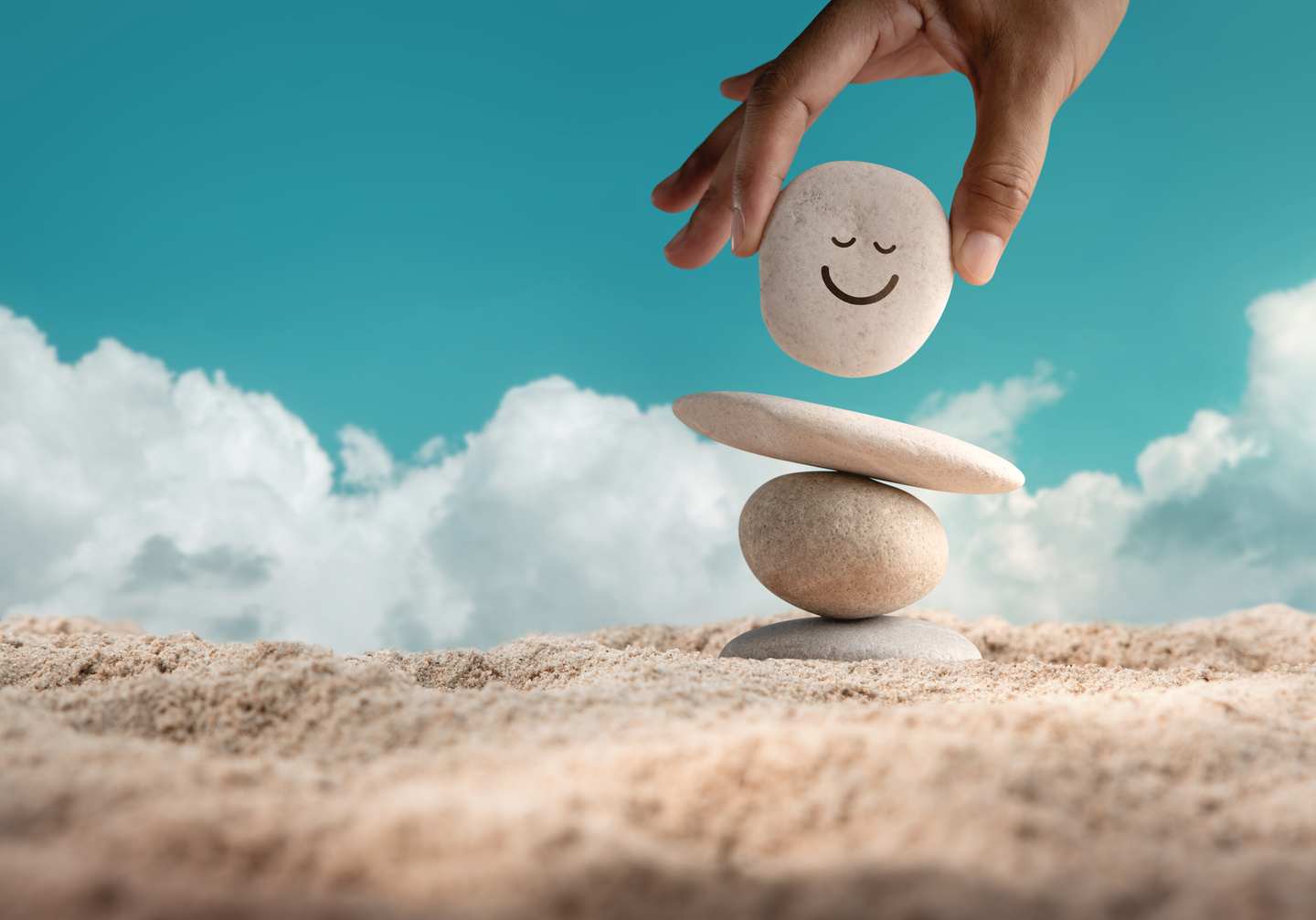 Person's Hand Stacking Pebbles with Smiley on Sand