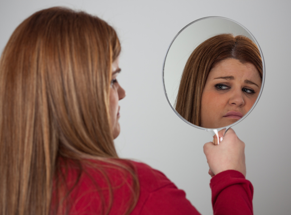 Woman with low self esteem disapproves her looks on mirror