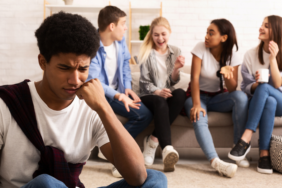 Upset bullied guy sitting alone, excluded by bad friends
