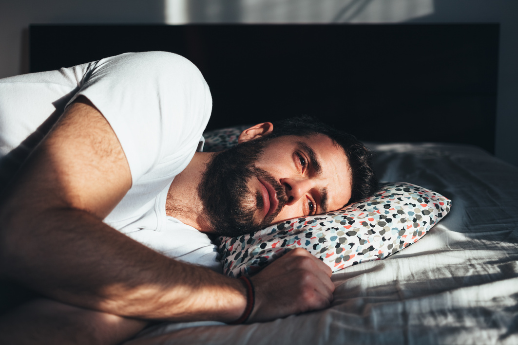 Young depressed man crying in bed